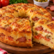 Lanche de forno dourado em formato de bolo com furo central, recheado com calabresa, queijo derretido, tomate e azeitonas, com uma fatia cortada mostrando o interior macio.